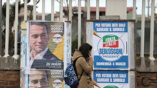 A woman passes electoral posters in Naples ahead of the polls opening