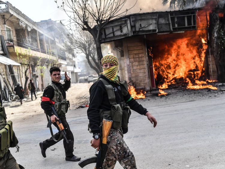 Turkish-backed Syrian rebels walk past a burning shop in Afrin