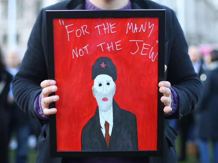 A demonstrator holding a painting saying "For the many not the Jew"
