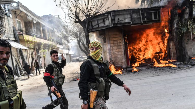 Turkish-backed Syrian rebels walk past a burning shop in Afrin