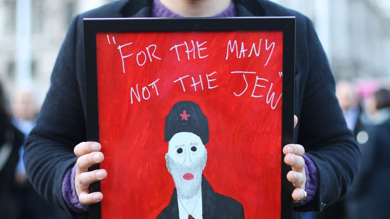 A demonstrator holding a painting saying "For the many not the Jew"
