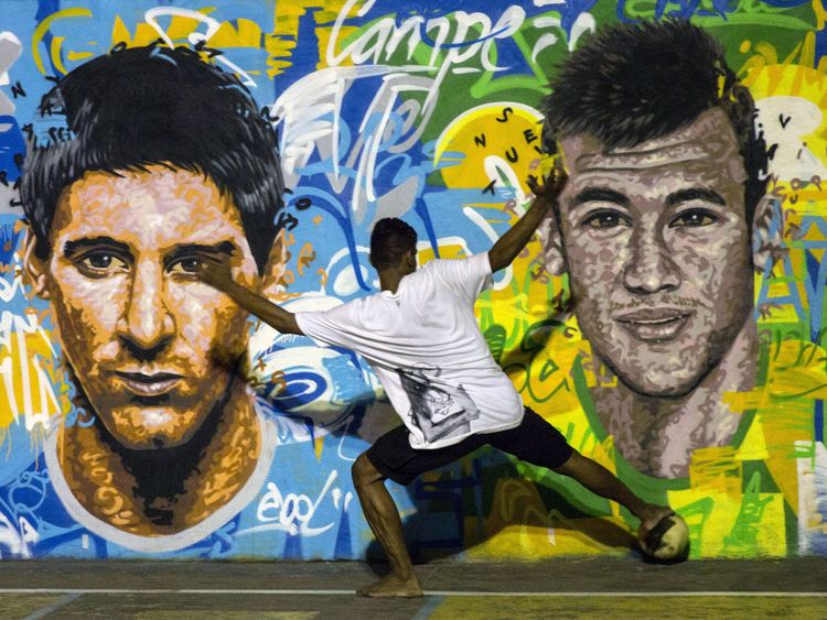 Youngsters play football in front of a mural of Argentine footballer Lionel Messi (L) and Brazil's Neymar