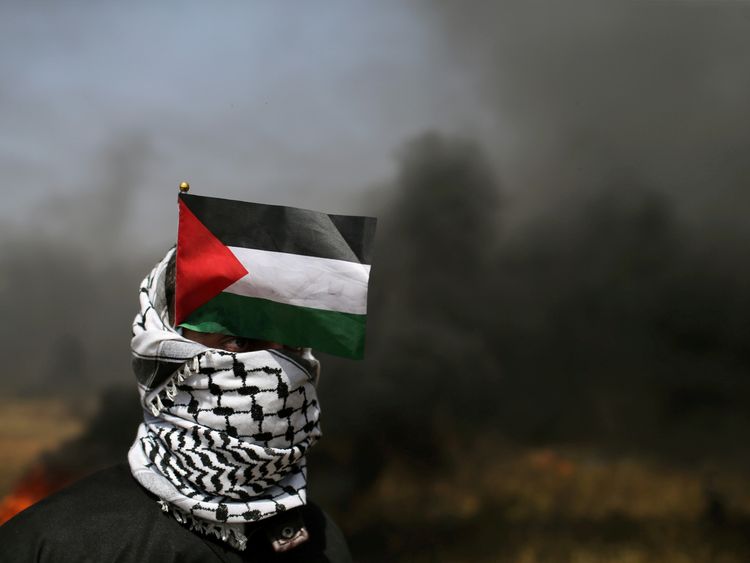 A demonstrator with a Palestinian flag looks on during clashes with Israeli troops