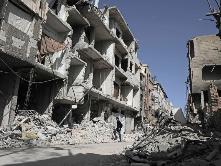 A Syrian man walks down a street past destroyed buildings on March 25, 2018, in Douma