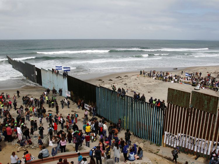 Asylum seekers stand on the Mexican side of the fence while their supporters cheer them on the US side
