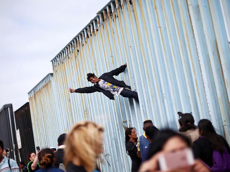 A man climbs the border fence in support of the hundreds of Central American migrants