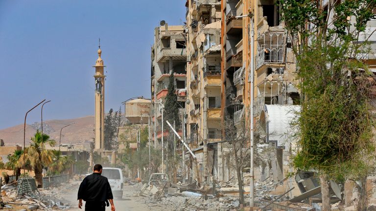 A picture taken during a Syrian army-organised tour on April 20, 2018 shows a man walking down a street past destruction in the Eastern Ghouta town of Douma on the outskirts of the capital Damascus