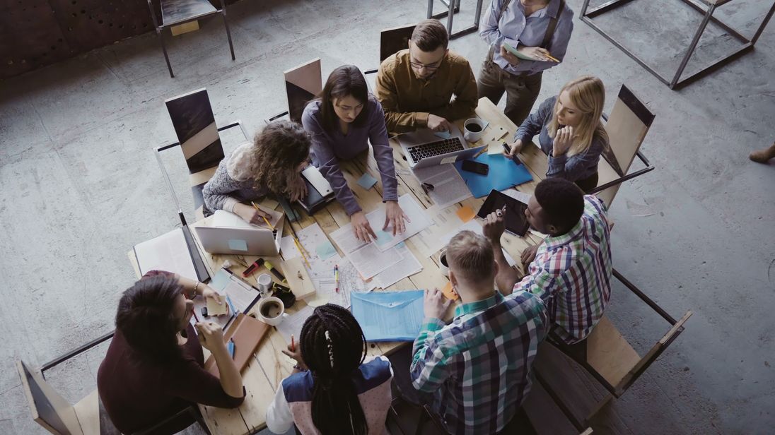 Top view of creative business team sitting at the table at loft office and working. Woman manager brings the document to mixed race group of people. Colleagues discussing the project.