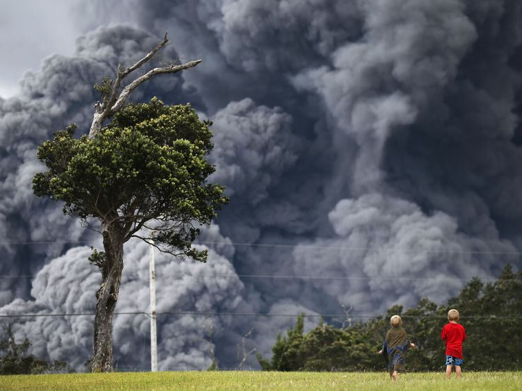 Boys look on from a  golf course as an ash plume rises in the distance