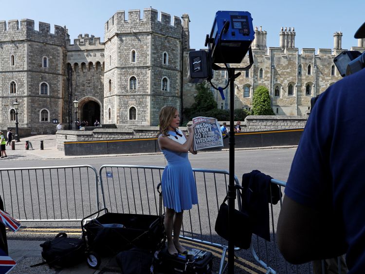 A television reporter for the US network CNN, holds up copies of today's British newspapers leading with a story of Meghan Markle's father Thomas Markle, opposite the Henry VII Gate of Windsor Castle in Windsor