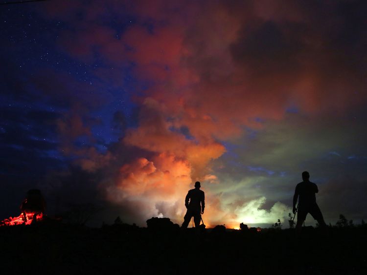 Photographers look on as lava from active fissures illuminates volcanic gases