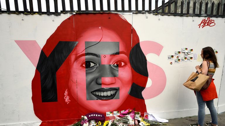 A woman looks at a new mural of Savita Halappanavar with flowers placed beneath it put up on the day of the Abortion Referendum 