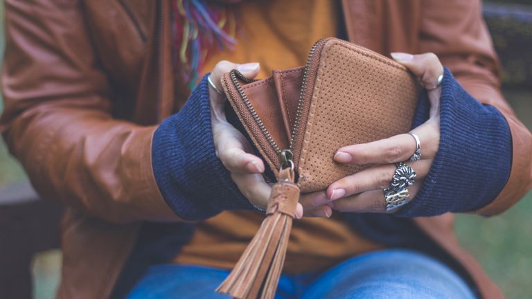 A young woman is holding her wallet outdoors in autumn park in city