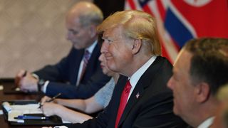 Donald Trump smiles as he looks at Kim Jong Un from across the table