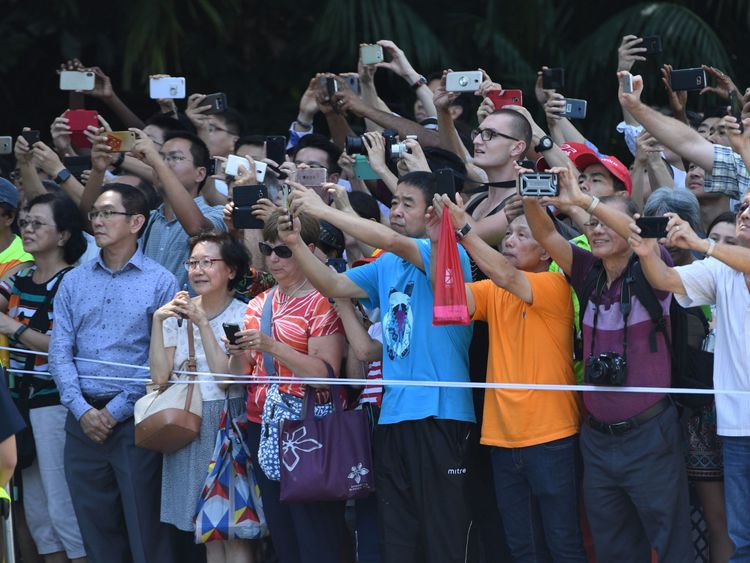 ystanders look on and take pictures of the motorcade transporting US President Donald Trump (not pictured) as it drives towards the Istana, the official residence of the Singaporean prime minister