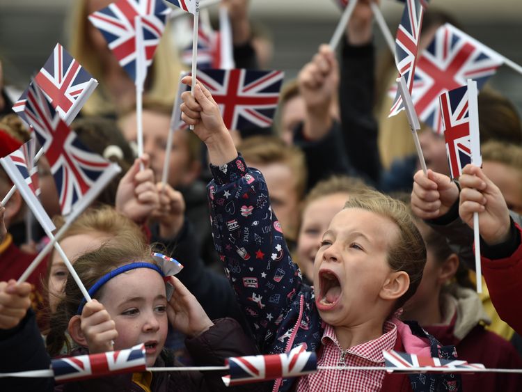 Schoolchildren wave flags as they greet the Queen and Meghan