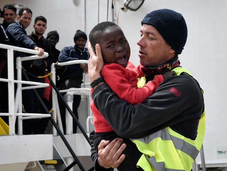 A helper from Doctors Without Borders (MSF) holds a Nigerian child as he and his mother (unseen) disembark from the MV Aquarius upon its arrival at the Sicilian port of Messina last month