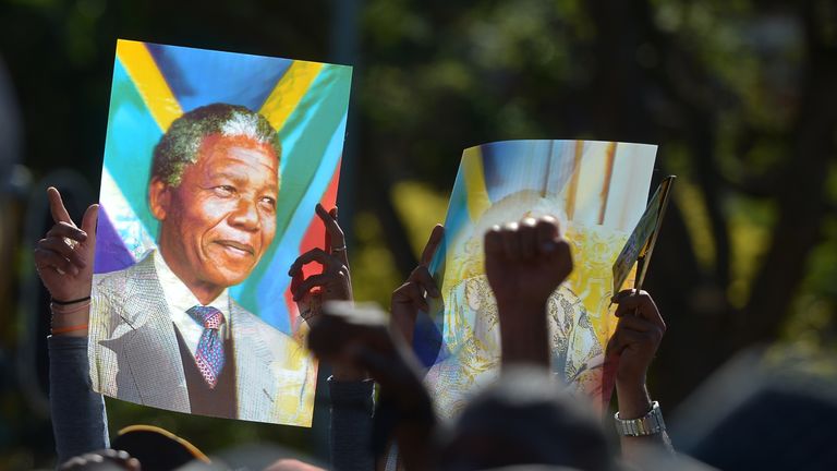 People hold a portrait of Nelson Mandela as they stand in line to pay her respect to South African former president Nelson Mandela lying in state at the Union Buildings on December 12, 2013 in Pretoria