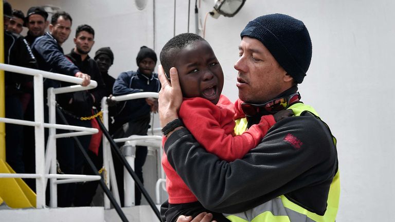 A helper from Doctors Without Borders (MSF) holds a Nigerian child as he and his mother (unseen) disembark from the MV Aquarius upon its arrival at the Sicilian port of Messina last month