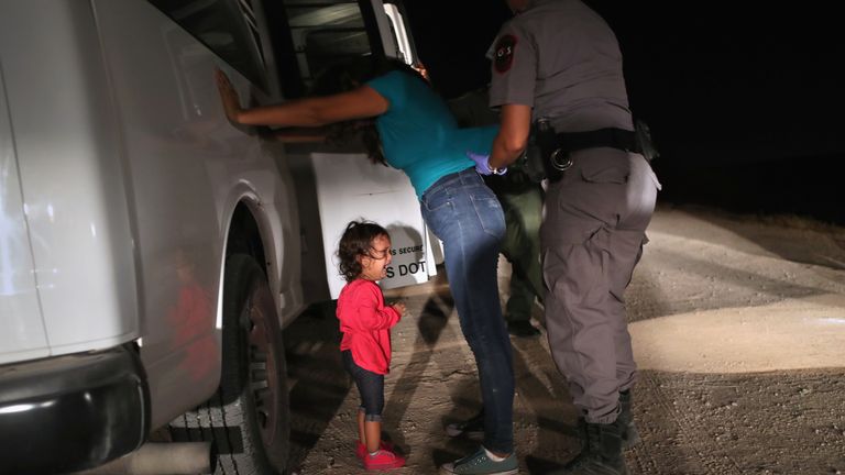 A toddler cries as her mother is searched at the border