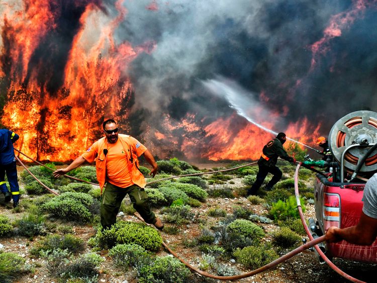 Firefighters and volunteers try to extinguish flames during a wildfire at the village of Kineta, near Athens