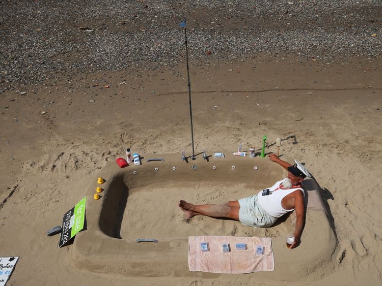 Ron 'The Beach Captain' poses in his 'shower' sand sculpture on the banks of the River Thames in London