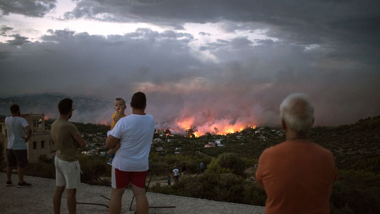 People watch the fires burn from a hilltop above Mati, Greece 