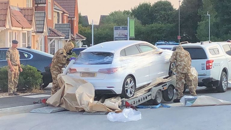 A car is wrapped in plastic film by personnel in military fatigues. Pic: James Street