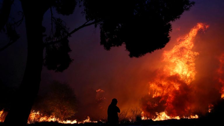 A man looks at the flames as a wildfire burns in the town of Rafina, near Athens, Greece, July 23, 2018. 