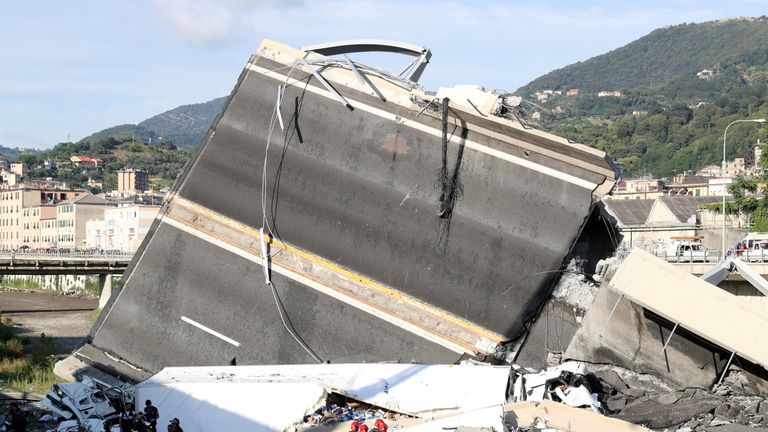 Rescue workers can be seen next to a large section of the fallen motorway