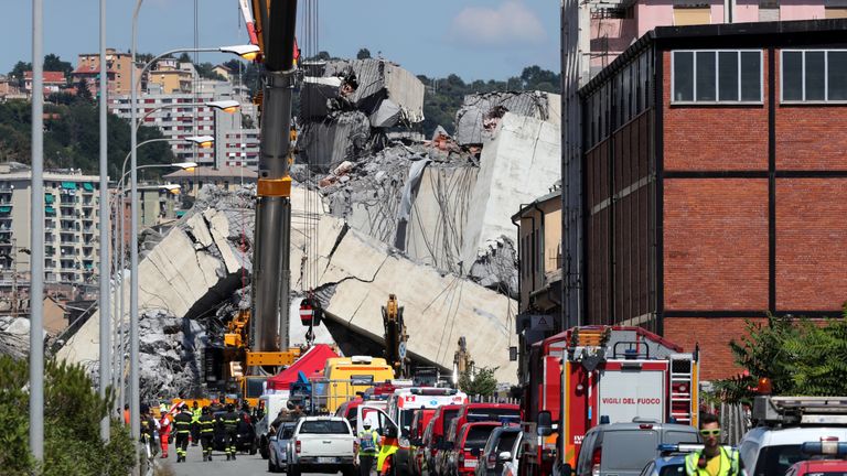 Firefighters and rescue workers stand at the site of the collapsed Morandi Bridge