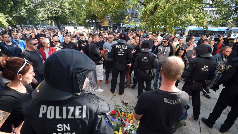 Riot police and citizens stand next to a makeshift memorial for a man who was stabbed to death