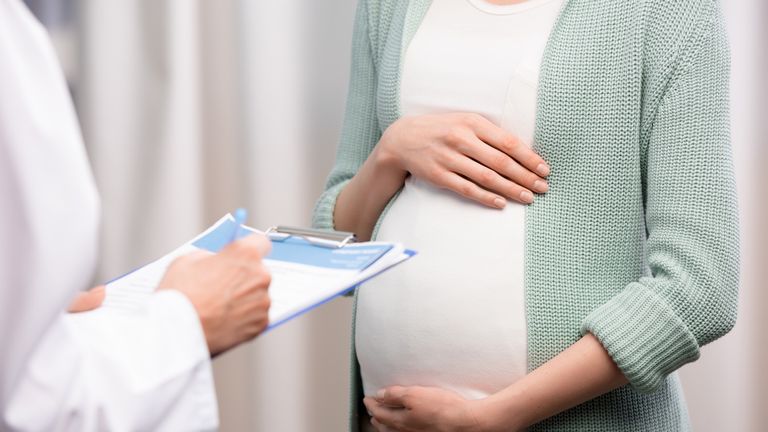 cropped shot of doctor writing down while pregnant woman holding stomach