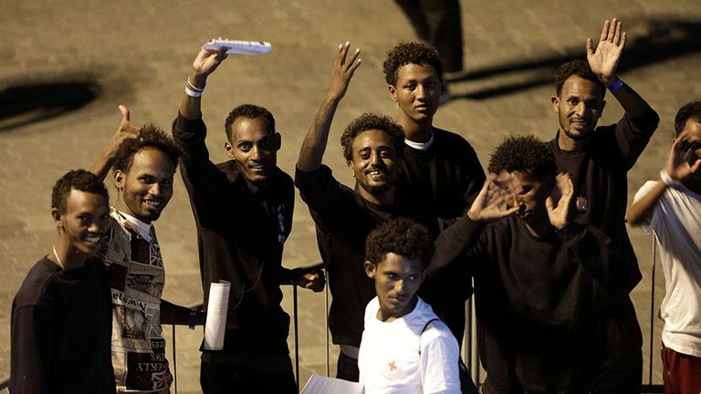 Migrants wave after being allowed to leave the ship