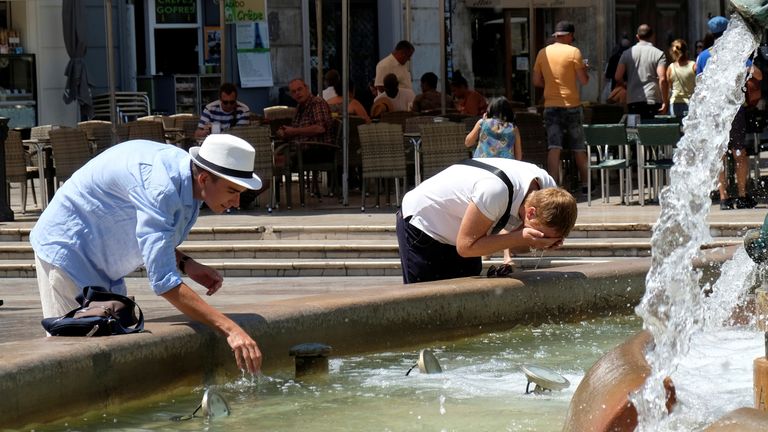 Tourists cool off at a fountain during the heatwave at the Virgin Square in Valencia, Spain
