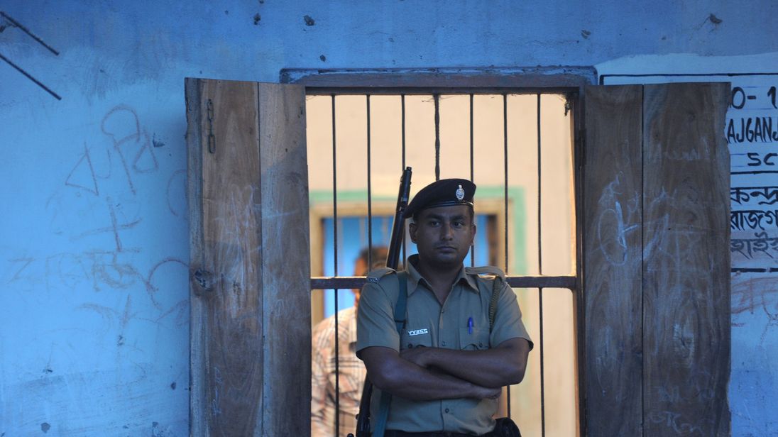 An Indian policeman stands guard outside a polling station as polling worker seal a box containing an Electronic Voting Machine ( EVM) after the polls closed at a polling station in Siliguri on April 17, 2014