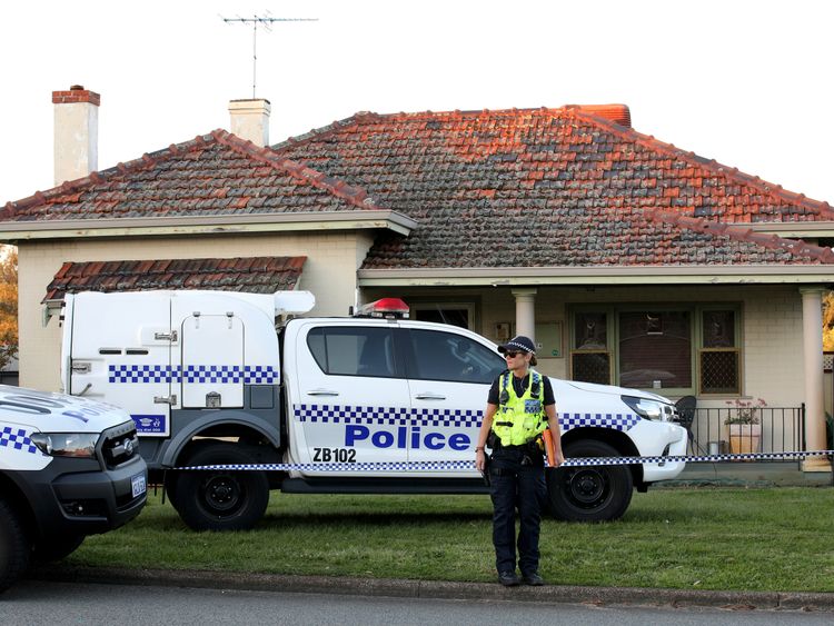A police officer stands outside a property where five people were found dead in a suburb of Perth, Australia