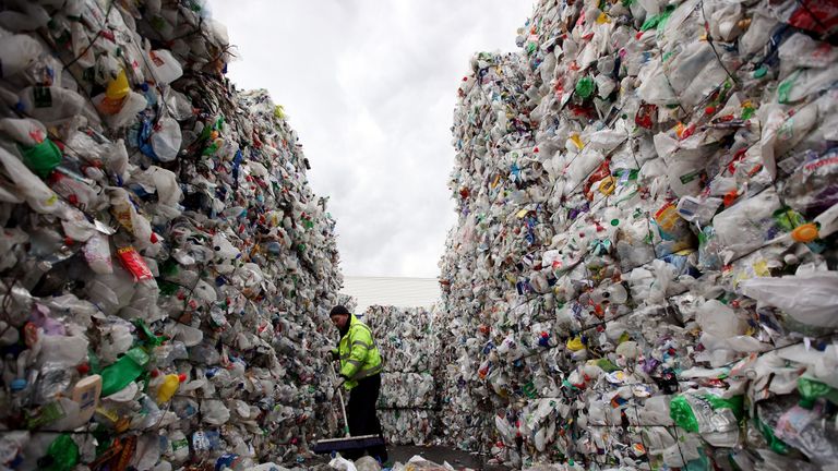 A recycling plant employee in London sweeps from inside a stack of plastic bottles