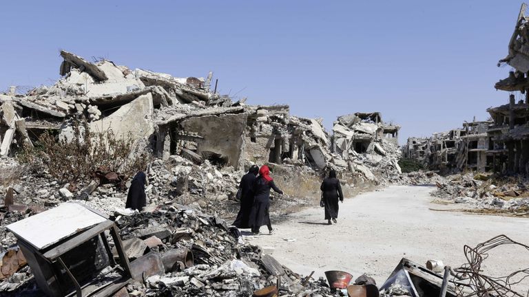 Three women walk among destroyed buildings in Homs