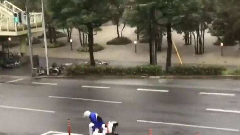 A dedicated pizza delivery worker struggling on a scooter in strong winds on the streets of Osaka