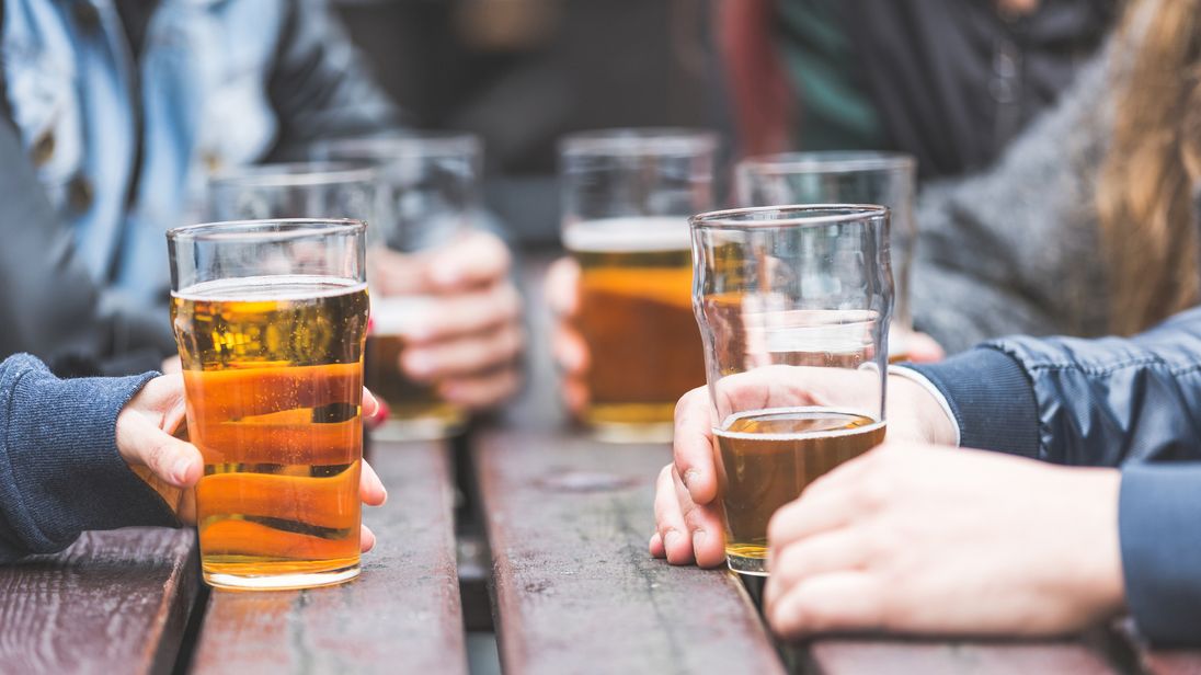 Hands holding glasses with beer on a table at pub in London. A group of friends is enjoying beer time in the city close up on the glasses