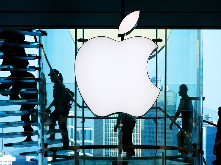 Employees walk past the big Apple sign in front of a shop