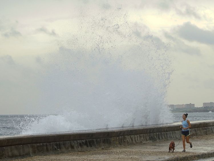 A woman jogs with a dog as waves splash at the seafront in Havana, after Hurricane Michael passed in western Cuba, October 9, 2018