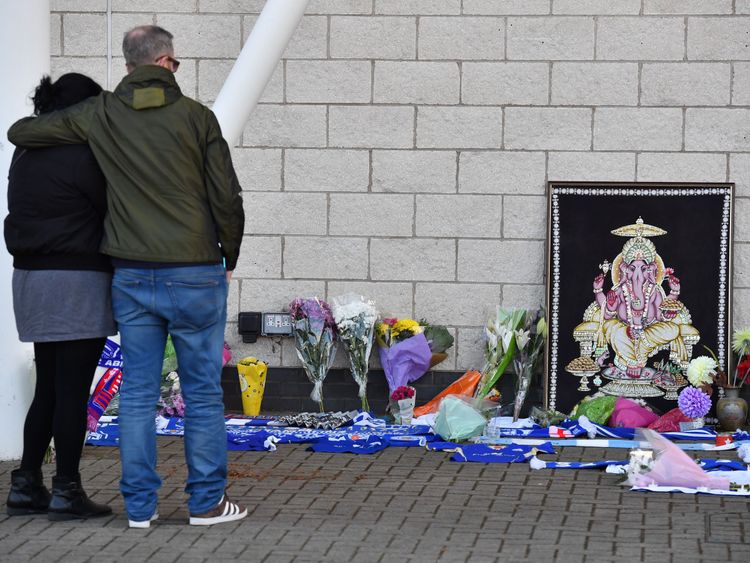 People react as they pause at floral tributes lined up outside Leicester City Football Club's King Power Stadium in Leicester, eastern England, on October 28, 2018 after a helicopter belonging to the club's Thai chairman Vichai Srivaddhanaprabha crashed outside the stadium the night before. - Leicester City's charismatic Thai chairman was the subject of growing concerns on October 28 after a helicopter belonging to the billionaire crashed and burst into flames in the stadium carpark shortly afte