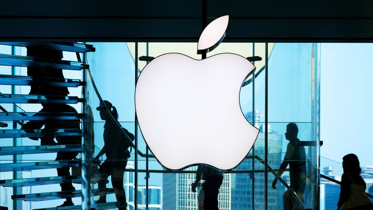 Employees walk past the big Apple sign in front of a shop