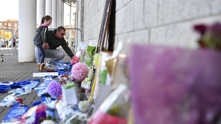 A man and a girl add to flowers and Leicester City scarfs left as tributes 