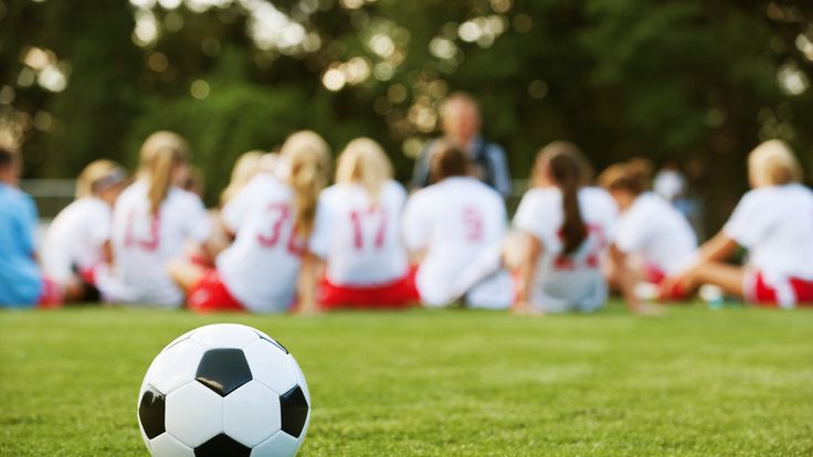 Close-up of soccer ball with girls soccer team in the background listening to coach.
