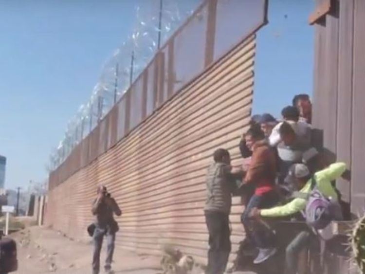Migrants break through a small gap in a fence before US border patrol fire tear gas at them
