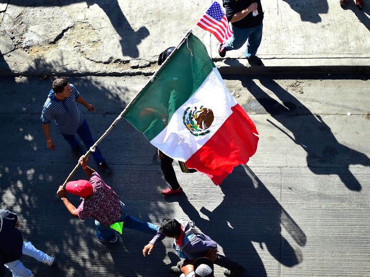 Migrants carry a Mexican and a US flag as they try to get to El Chaparral border crossing