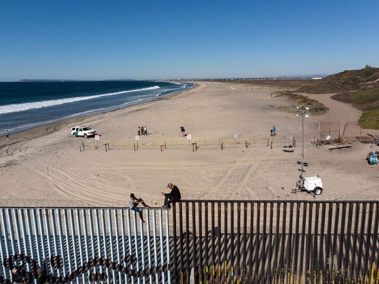 Two members of the migrant caravan sit on the US border fence before it is sealed